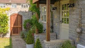 Une maison en pierre avec une porte en bois, une porte blanche et un petit porche agrémenté de plantes en pot.