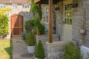 A stone house with a wooden door, a white door, and a small porch with potted plants.