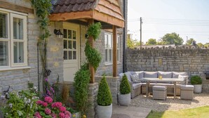 Une maison en pierre dotée d’un patio avec un salon de jardin comprenant un canapé et des plantes en pot.