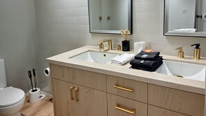 A modern bathroom with a dual sink, gold handles, and a large mirror.