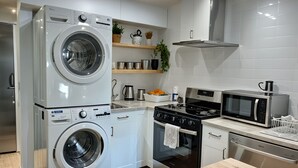 A modern kitchen with a stacked washer and dryer, a stove, microwave, and a dishwasher.