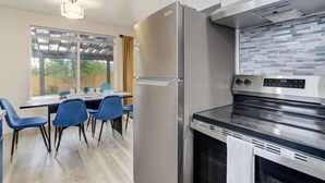 Una cocina moderna con un refrigerador de acero inoxidable, un horno empotrado y una zona de comedor con sillas azules y una mesa.