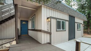 Una casa con puerta azul, el número '2115' en la pared y una terraza de madera.