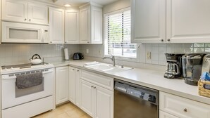 A modern kitchen with white cabinetry, a built-in microwave, a coffee maker, and a dishwasher. - Golf & Swim: Country Club Condo in Palm Desert (Palm Desert)