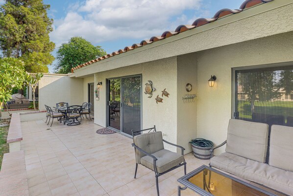 Un espace extérieur aménagé en patio, avec une table et des chaises pour les repas, un banc rembourré et une table avec un plateau en verre.