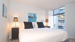 Een slaapkamer met een groot bed, twee nachtkastjes met lampen, een schilderij aan de muur en een raam met uitzicht op een balkon.