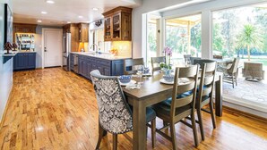 A spacious kitchen with wooden cabinets, a dining area with a table and chairs, and large windows offering a view of the outdoors.