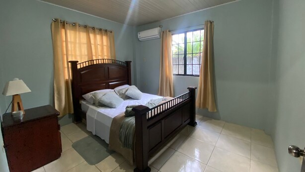 A bedroom with a wooden bed, a nightstand, a lamp, and a window with curtains. - Relaxing, family-friendly 2-bedroom apartment with A/C, WiFi & Central Location (Golconda)