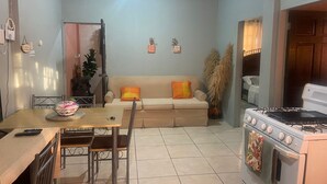 A compact living space with a dining area, a sofa with cushions, a kitchen with a stove, and a tiled floor. - Relaxing, family-friendly 2-bedroom apartment with A/C, WiFi & Central Location (Golconda)