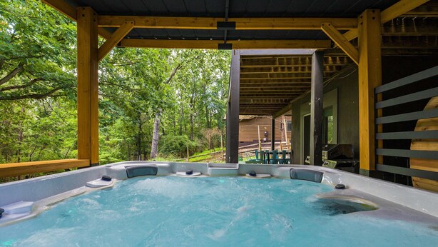 A hot tub area with a wooden deck and a view of a forest.