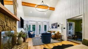 A spacious living room with a stone fireplace, a blue armchair, and a wooden ceiling.