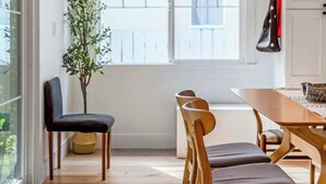 A dining area with a wooden table and chairs, a potted plant, and a view through a window.