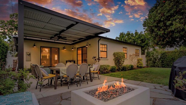 A modern house with a patio area featuring a fire pit, outdoor seating, and a covered dining area.