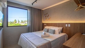 Quarto de hotel com uma cama grande, uma escrivaninha de madeira e vista para palmeiras pela janela.