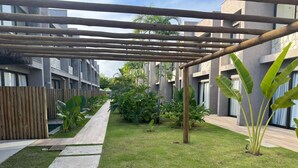 Um pátio com pérgola de madeira, calçada pavimentada e vegetação exuberante.