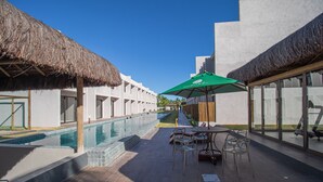 Área de piscina com telhado de palha, piscina e mobiliário para áreas externas.