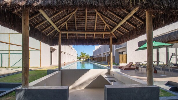 Uma área de piscina com estrutura de telhado de palha, espreguiçadeiras e vista desimpedida da piscina.