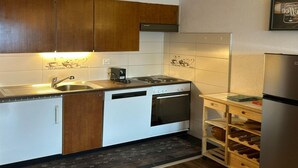 A compact kitchen with wooden cabinets, a built-in dishwasher, a stove, and a wine rack.