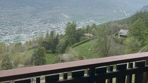 A panoramic view of a mountainous landscape with a town below, a river, and a small cabin on the hillside.