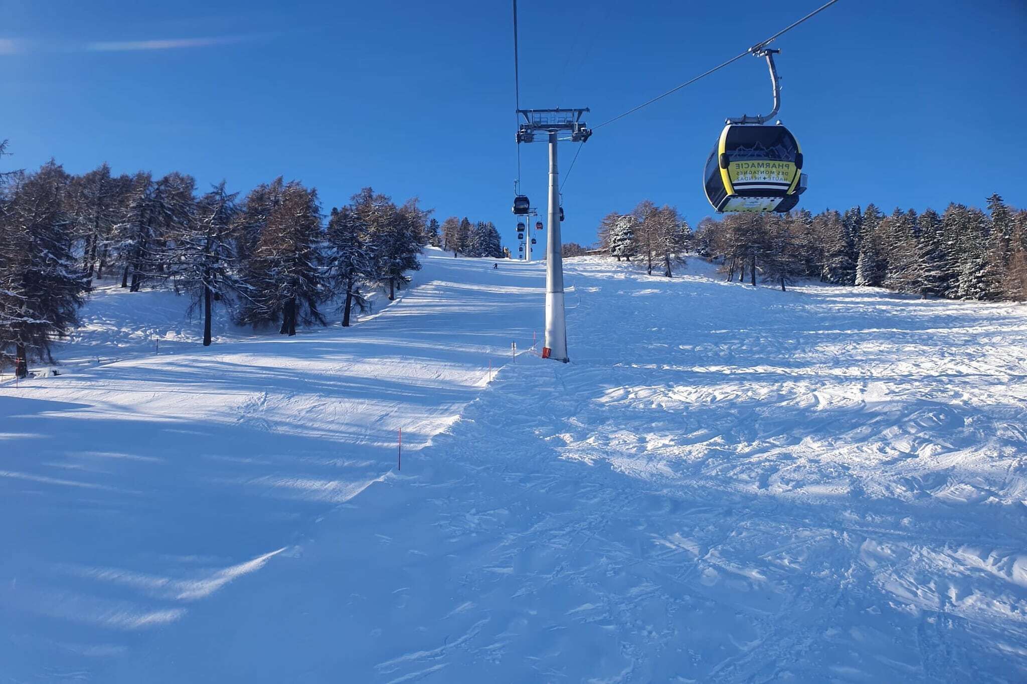 A ski lift chair suspended above a snowy slope with trees in the background.