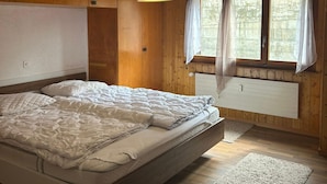 A bedroom with a bed, wooden walls, a window with curtains, and a hanging light fixture.
