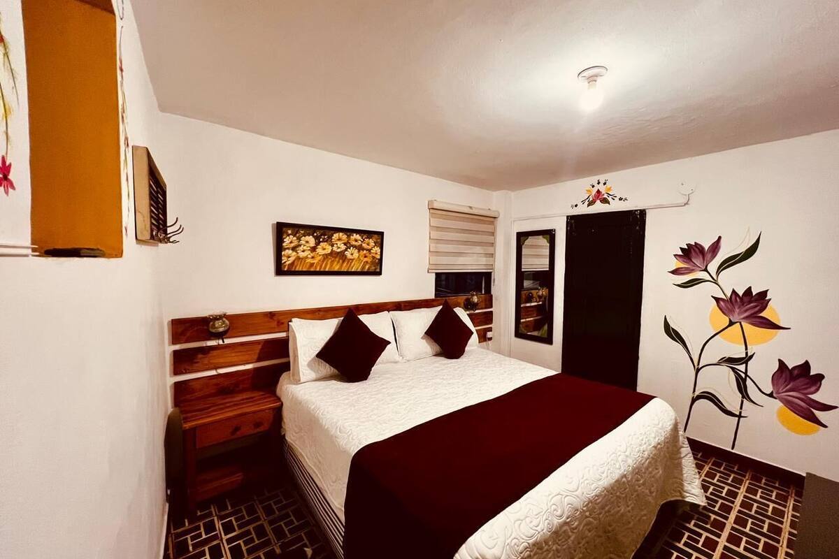 Ein Schlafzimmer mit einem Bett, einem Holzkopfstück, einem Nachttisch, einer Kommode und einer Wand mit einem Blumenbild.