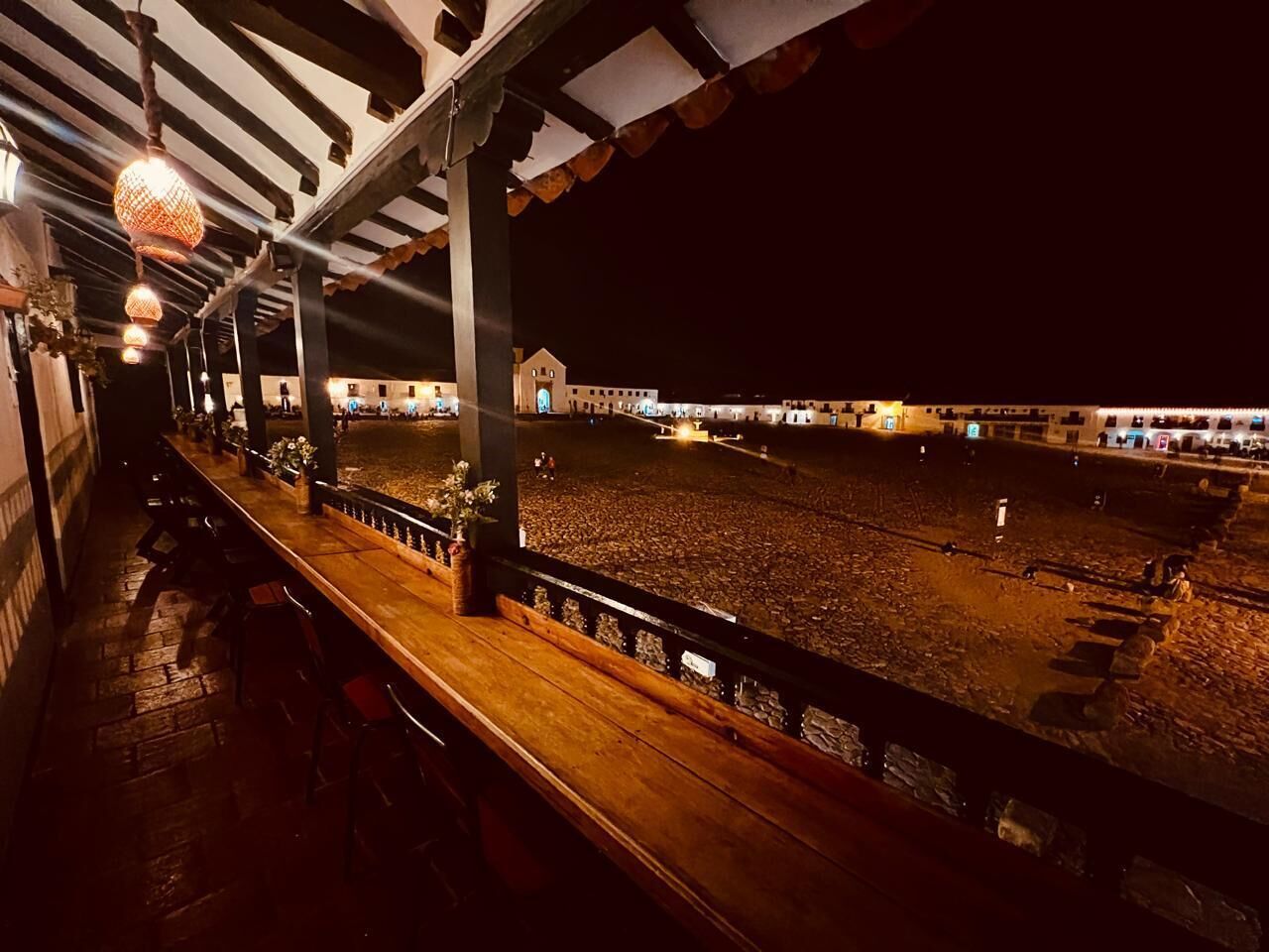 An outdoor seating area with wooden benches and a railing, overlooking a large open space with a building in the background.