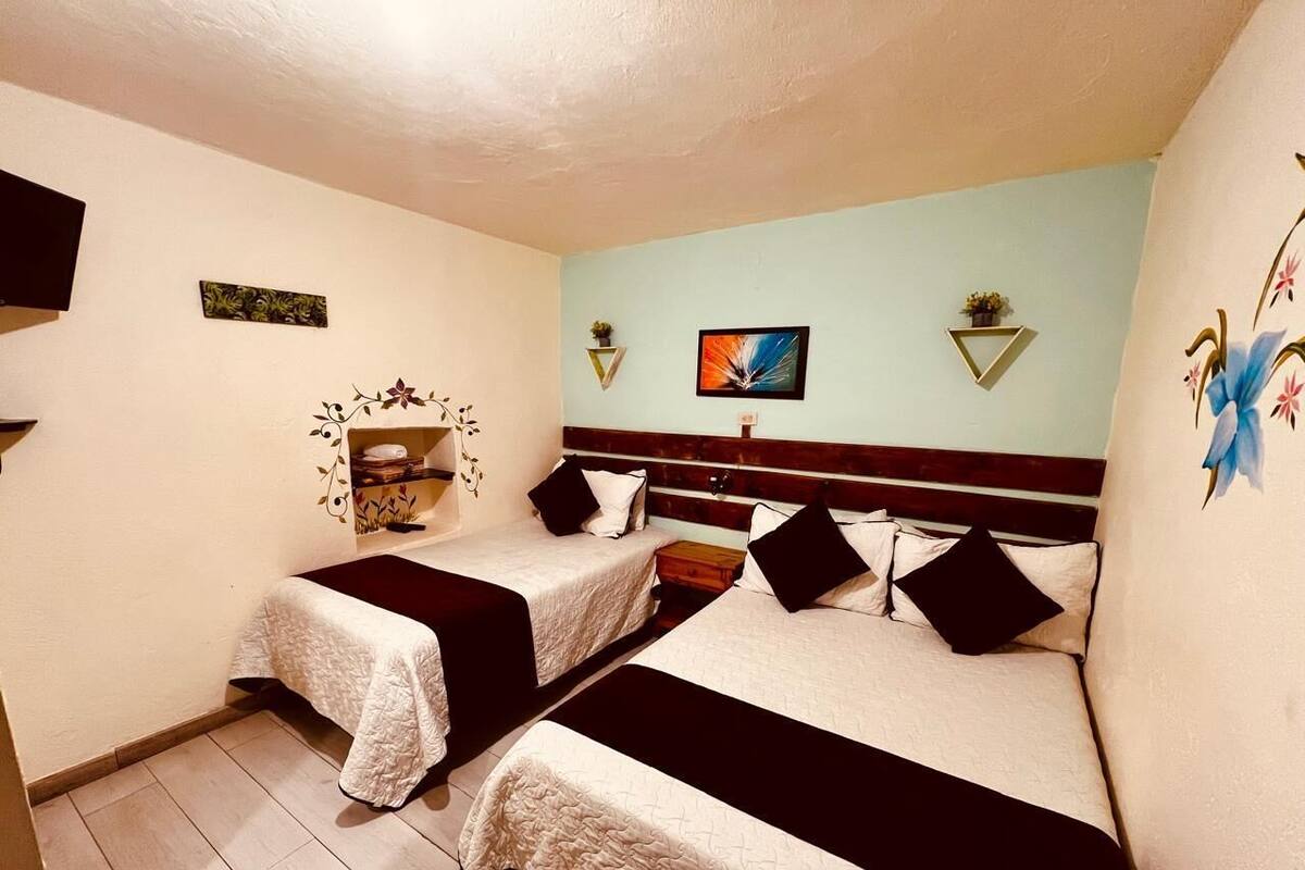 Ein Zimmer mit zwei Betten, jeweils mit einer schwarz-weißen Tagesdecke, einem Holzkopfstück und einem kleinen Tisch dazwischen.
