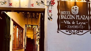A hallway with a staircase leading to a door, a wall-mounted sign for Hotel Balcon Plaza, and decorative elements like flowers and leaves. - Balcon Plaza Villa de Leyva Hotel (Villa de Leyva)