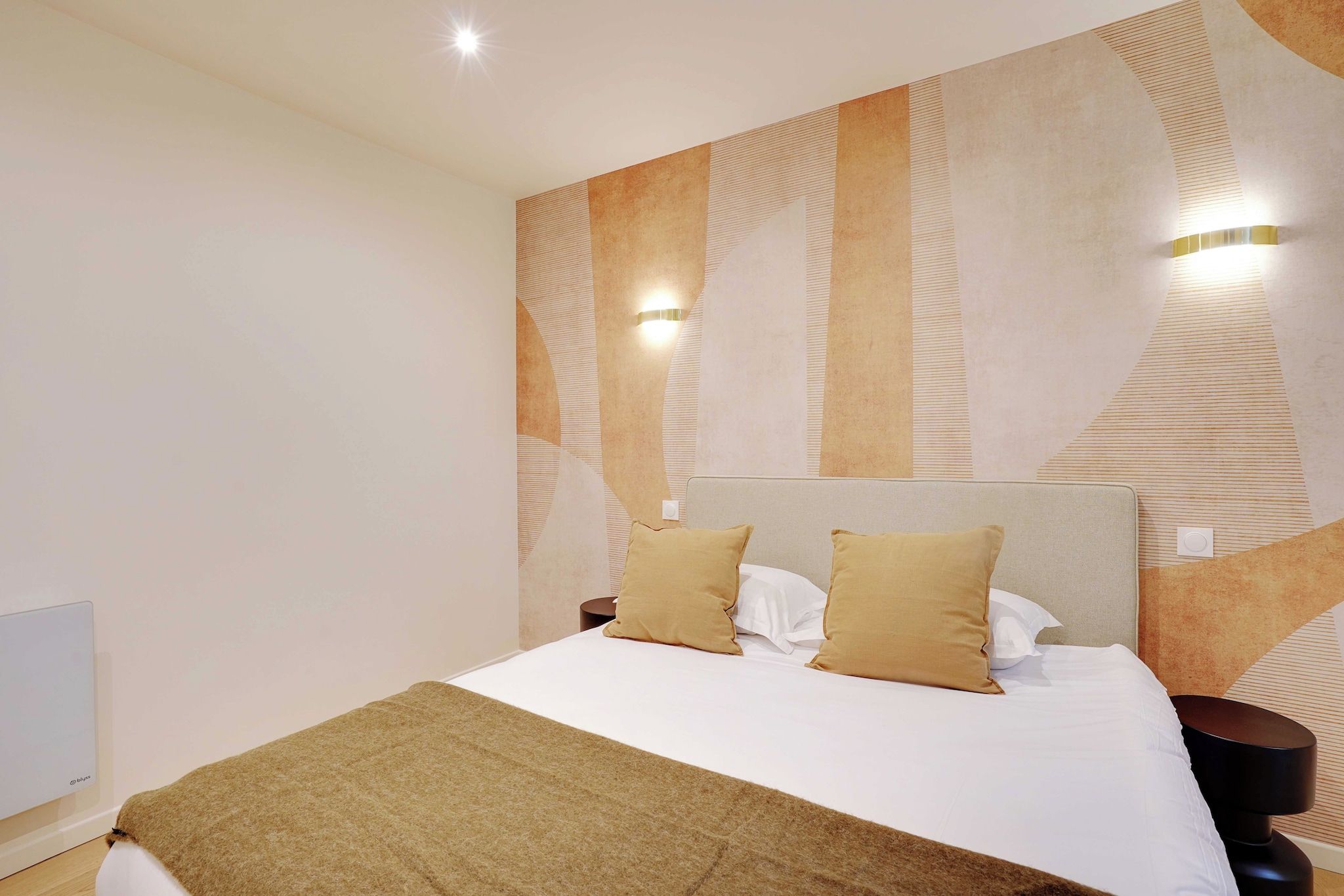 A modern hotel room with a large bed, two bedside tables, and a wall with a geometric pattern.