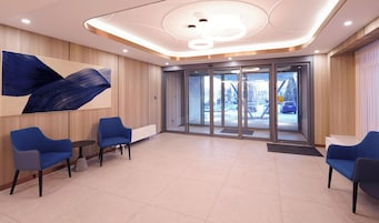 Una hall moderna con un grande dipinto astratto, posti a sedere blu e una porta vetrata che dà sull'esterno.