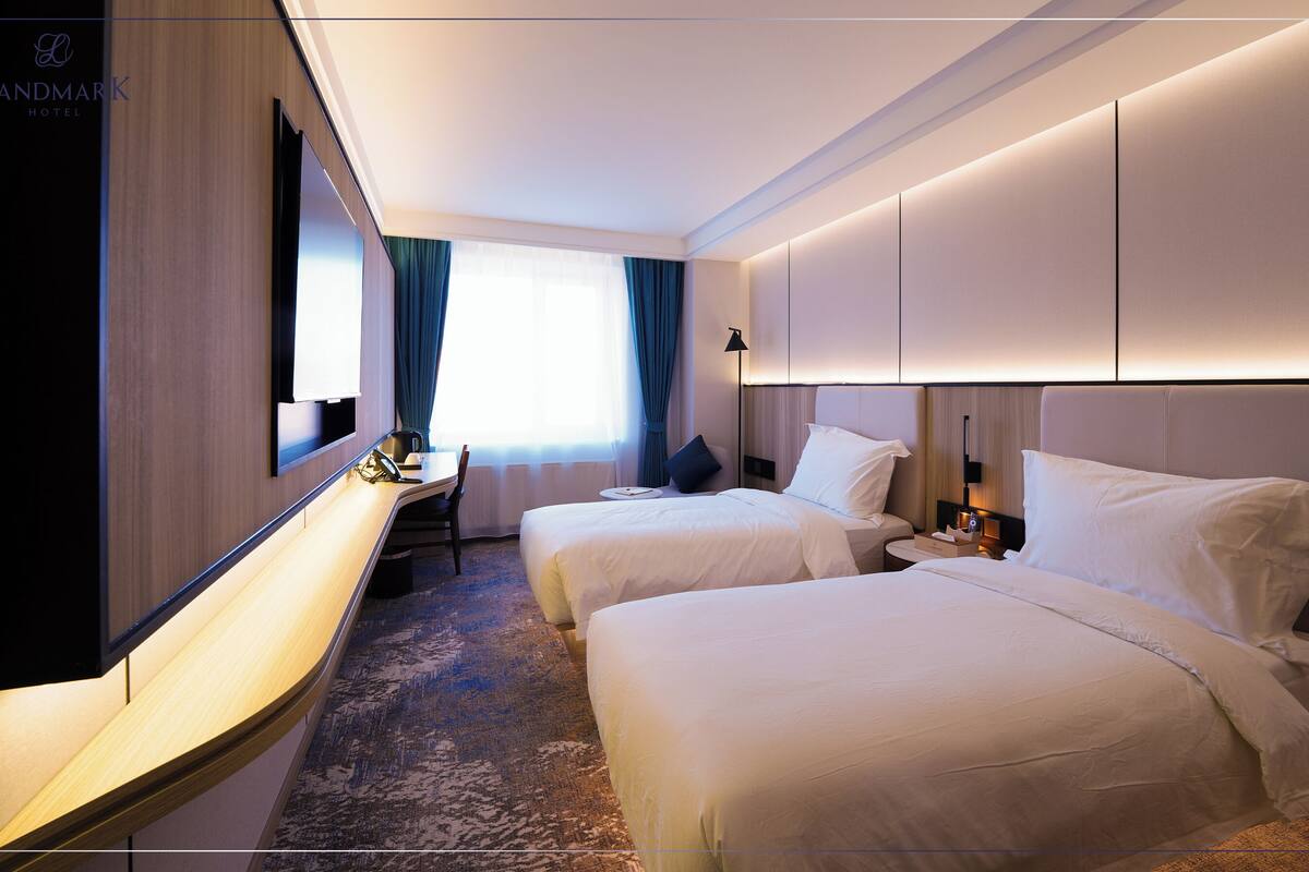 Habitación de hotel con dos camas, un escritorio, una silla, un televisor y un espejo grande.