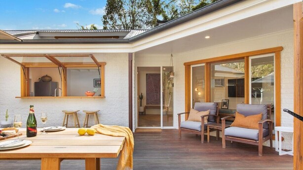Une maison moderne dotée d’une terrasse en bois, d’un coin repas avec une table et des chaises, et d’un salon avec des canapés et un téléviseur.