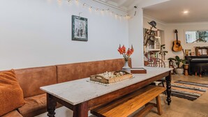 Un salon chaleureux avec un canapé marron, une table en bois sur laquelle est posé un jeu d’échecs, et une guirlande lumineuse accrochée au plafond.