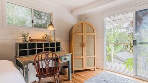 Une pièce avec un bureau en bois, une chaise, une bibliothèque, une grande porte en arc de cercle et une vue sur la verdure, visible à travers une porte-fenêtre coulissante.