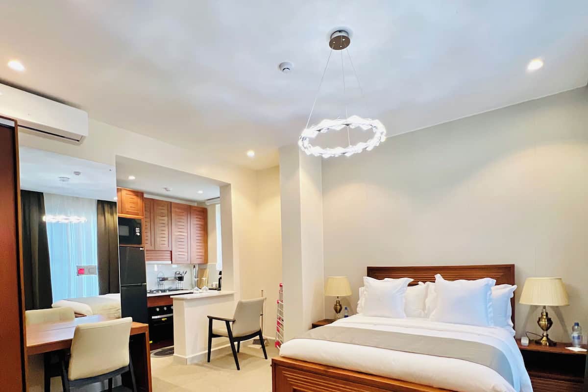 A hotel room with a wooden bed, a desk, a chair, a kitchenette, and a bathroom.