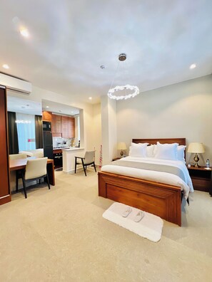 A hotel room with a wooden bed, a desk, a chair, a kitchenette, and a bathroom.