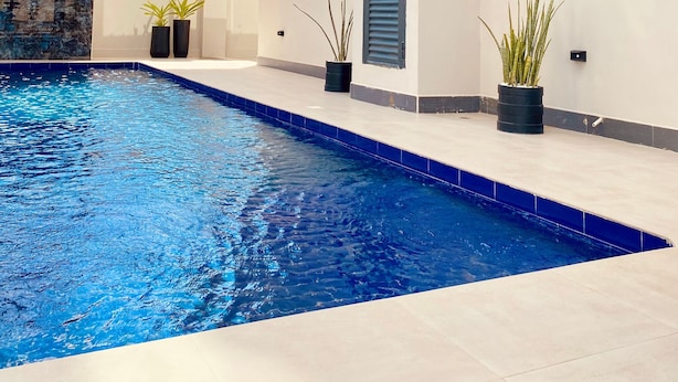 Un edificio moderno con una piscina, piante in vaso e un cielo azzurro limpido.