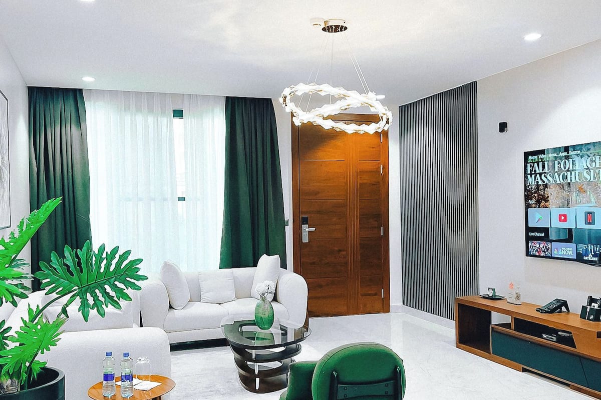 A modern living room with a white sofa, a green armchair, a round coffee table, and a TV mounted on the wall.