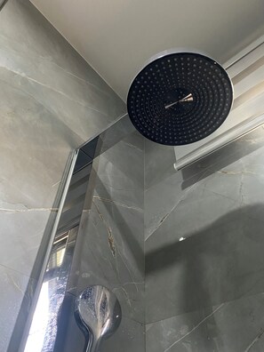 Una ducha con cabezal circular, desagüe visible y pared de azulejos con grietas.