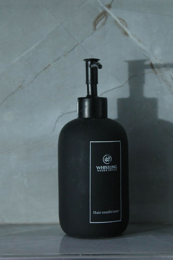 Un frasco negro de acondicionador para el cabello de Whisling Woods Hotels sobre una superficie reflectante.
