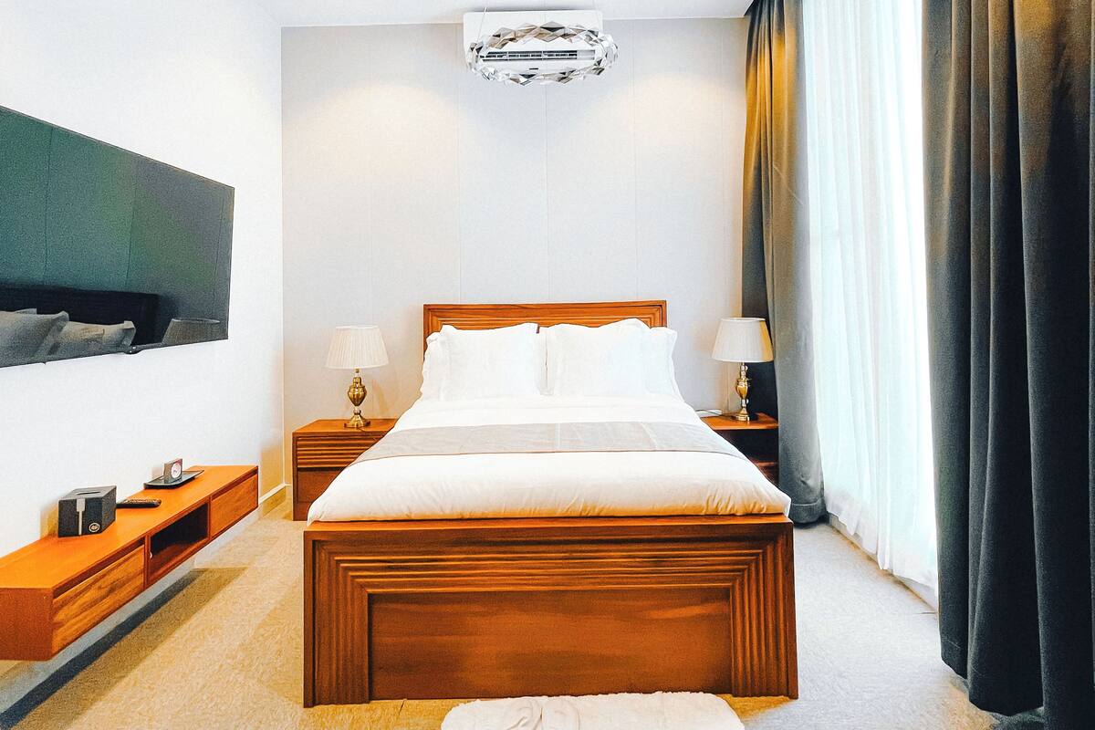 A modern hotel room with a large bed, bedside tables, a TV, and a chandelier.