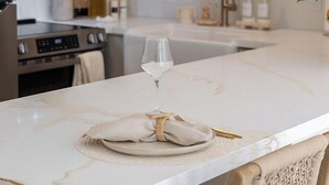 A marble dining table with a folded napkin, a glass of water, and gold cutlery. - Kaia Villa, at Turtle Bay - Modern North Shore Oahu Retreat w/Lanai & Golf Views (Kahuku)