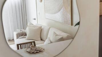A modern hotel room with a large mirror reflecting a neatly made bed, a white sofa, and a minimalist decor.