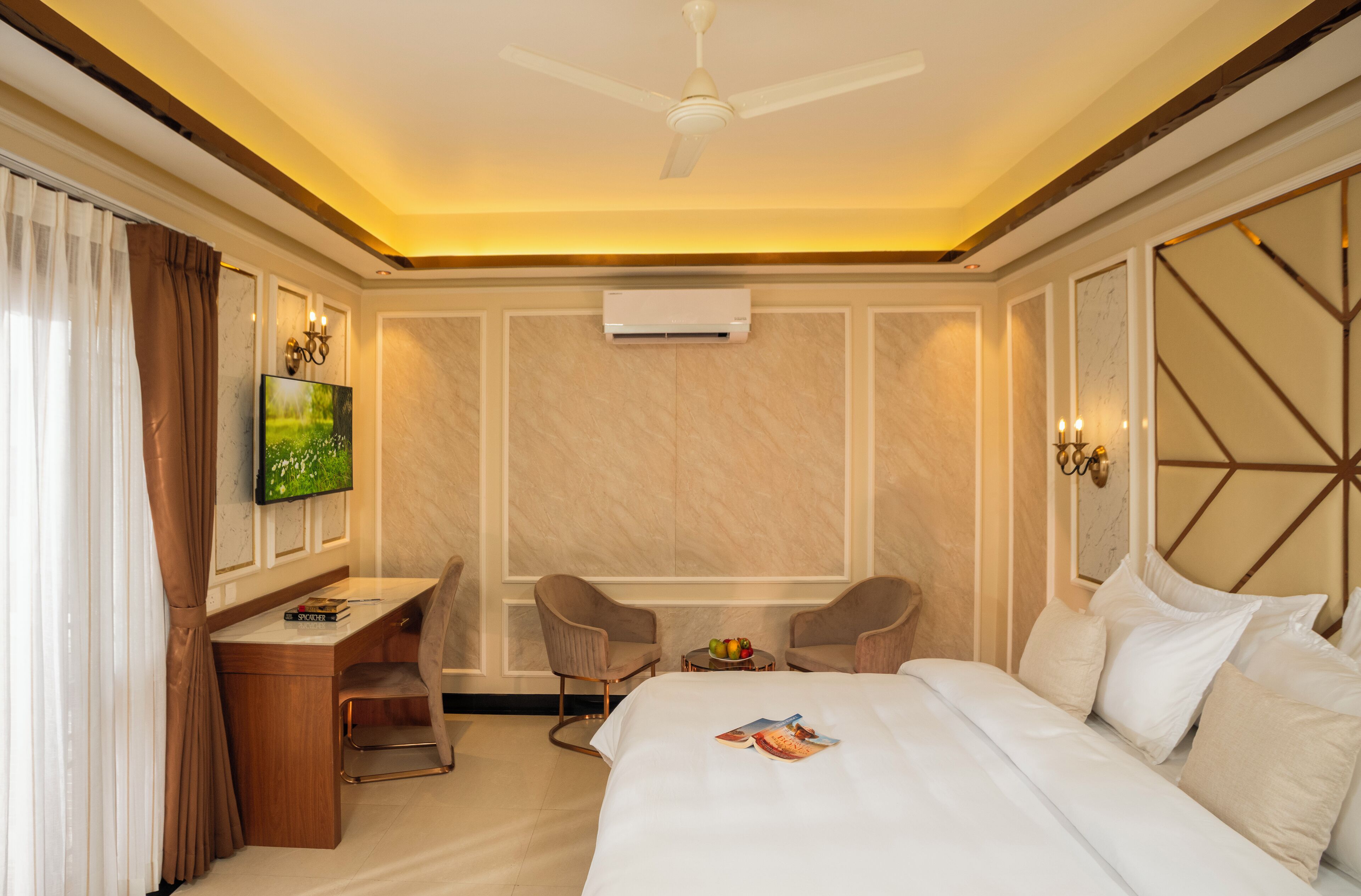 A hotel room with a bed, desk, two chairs, a TV, and an air conditioning unit.