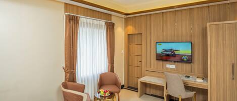 A hotel room with a bed, two armchairs, a small table with fruit, a desk with a chair, a television, and wooden paneling on the walls.