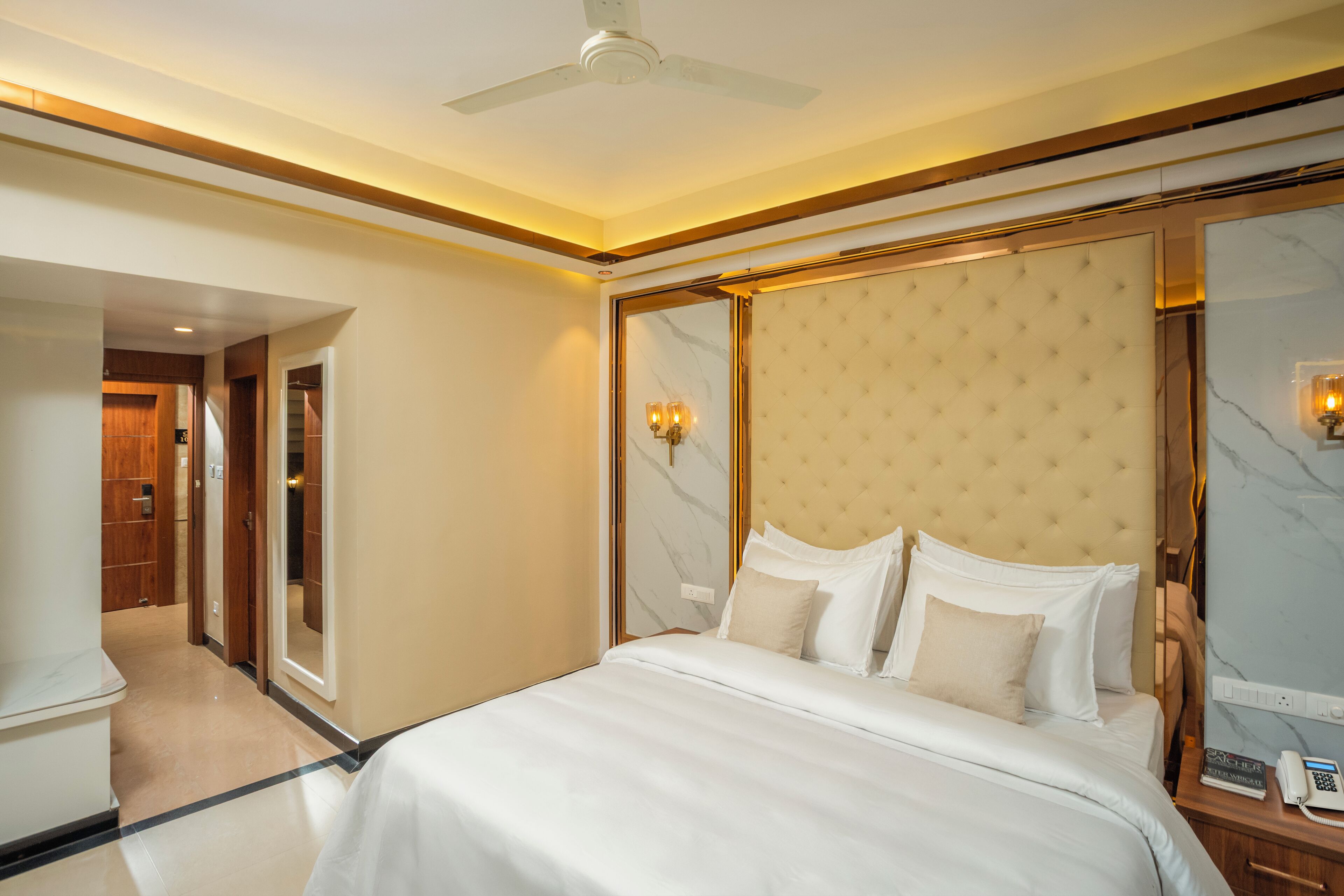 A hotel room with a large bed, a ceiling fan, a marble wall, and a wooden door.