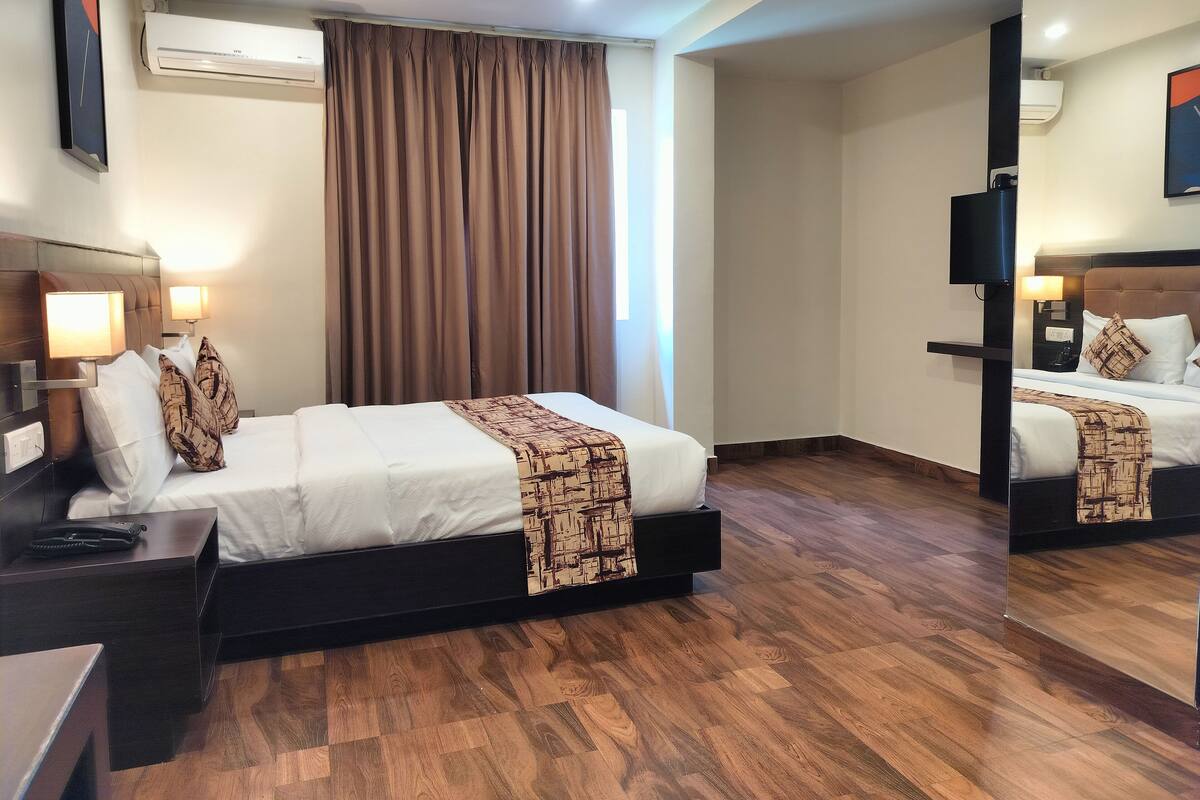 A hotel room with a bed, bedside tables, a lamp, a mirror, and a large window with curtains.