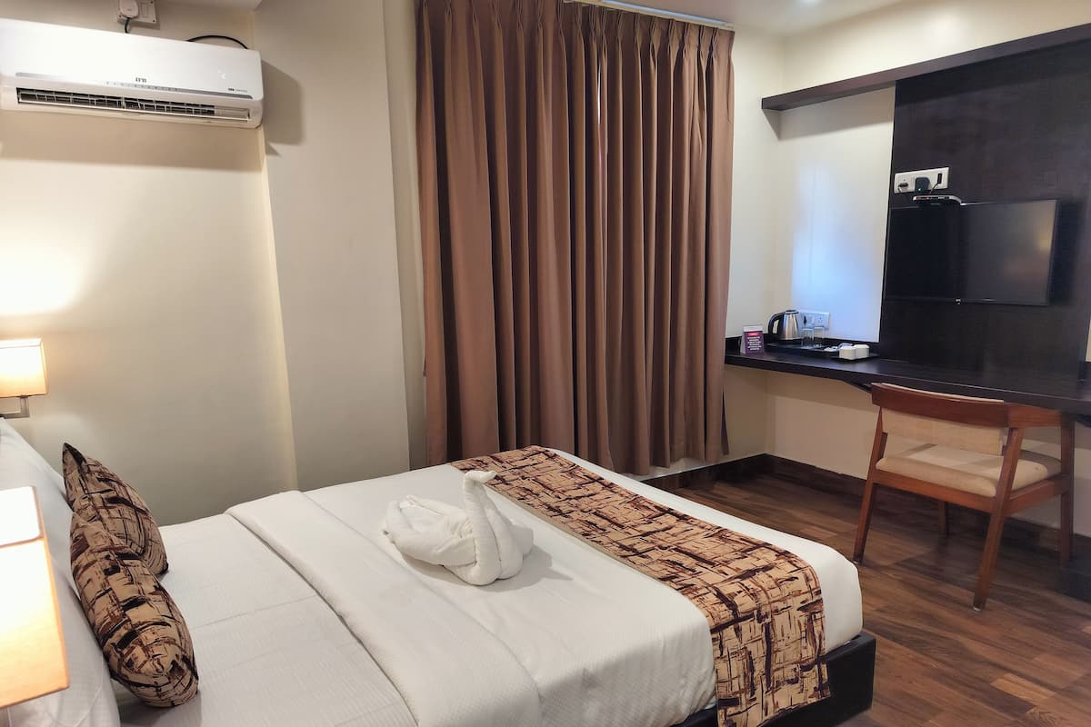 A hotel room with a bed, a desk, a TV, and an air conditioning unit.