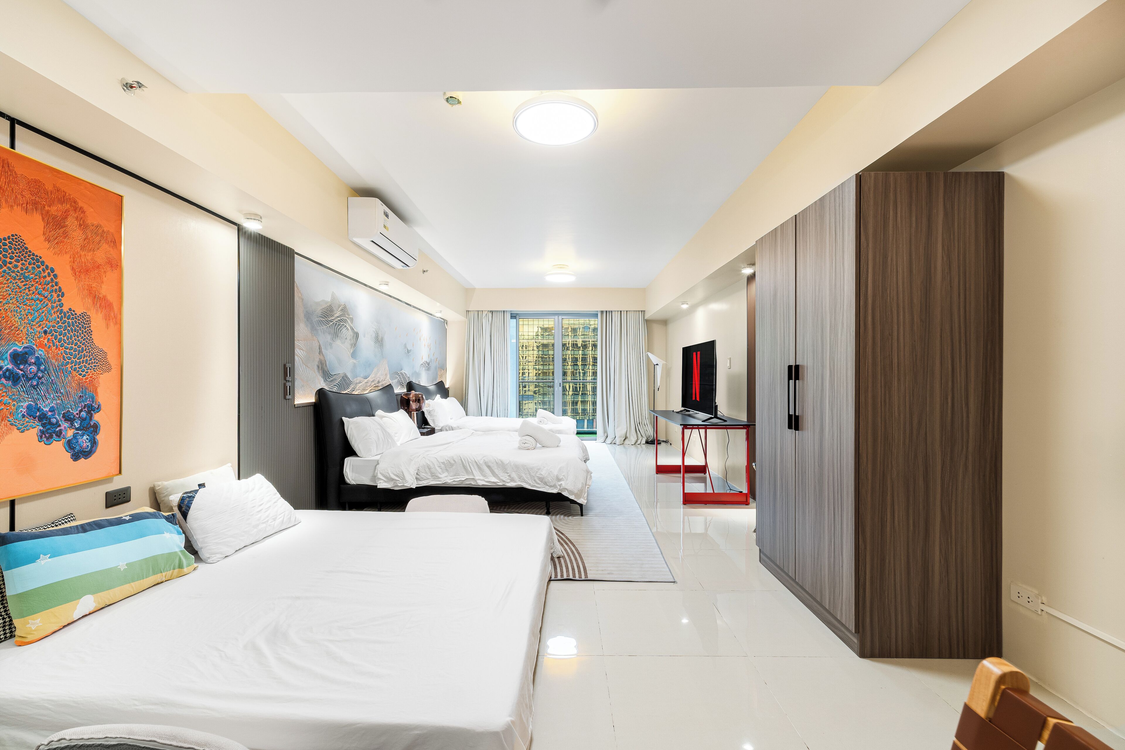 A hotel room with two beds, a large painting, a TV, and a wardrobe.